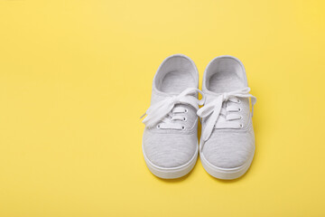 Pair of grey sneakers with tied shoelaces on yellow background