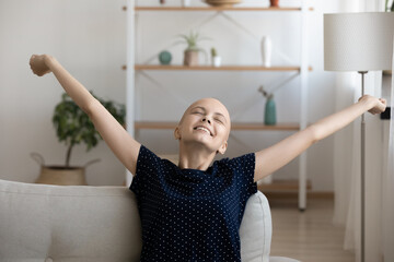 Close up smiling hairless woman stretching hands on couch, relaxing, enjoying lazy leisure time,...
