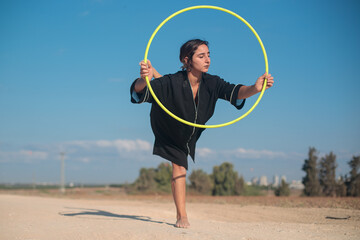 Female flow artist dancing with a Hula hoop outdoors, with one leg on the ground. Wide shot in natural morning sunlight.  © Calacuda_stock
