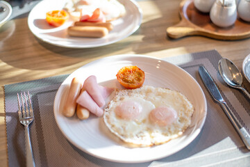 American Breakfast on the table consists of fried eggs, ham and sausage.