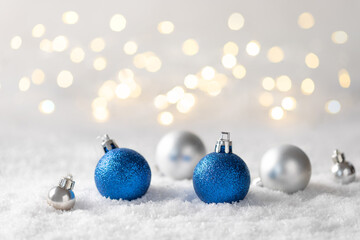 silver and blue Christmas decorations on the snow with blurred Christmas lights. greeting card