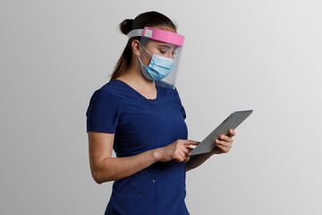 Mujer latina, con uniforme de enfermera usando cubrebocas y careta, sosteniendo una tableta digital en las manos, y un fondo color gris con espacio para texto
