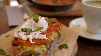 Healthy vegetarian Mediterranean brunch out. Avocado toast with poached egg and tomato paste on wooden plate with coffee