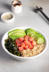 healhty lunch bowl with quinoa, salmon, wakame seaweed, avocado and cucumber. Diet food. Vertical image. grey background