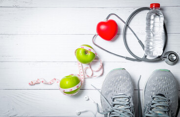 Running shoes with green apples and stethoscope near fresh water bottle