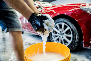 Worker washing red car with sponge on a car wash