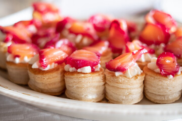 Bite sized finger food with smoked salmon and cream cheese filling in puff pastry. Buffet style catering table setting.