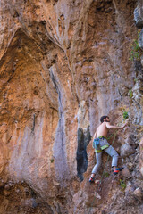 A strong man climbs a beautiful orange rock.