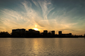 Obraz premium Rippled water surface of lake with city buildings silhouettes on the horizon at sunset