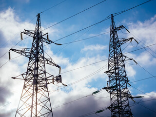 High voltage electricity pillars on the blue sky background with clouds. Metal bearing high voltage power line. High tech power lines