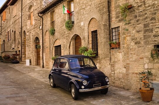 Fototapeta An alley of an Italian medieval village with an old car parked (Gubbio, Umbria, Italy)