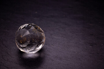 Faceted sphere, sparkling crystal on dark, black background. Large glass with light refraction, stone backdrop. Empty space for inscriptions