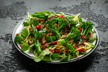 Tenderstem broccoli and egg noodles Asian style vegetarian salad with roasted pine nuts and pomegranate seeds