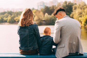 A family sitting on a bench and looking at a lake with a baby .