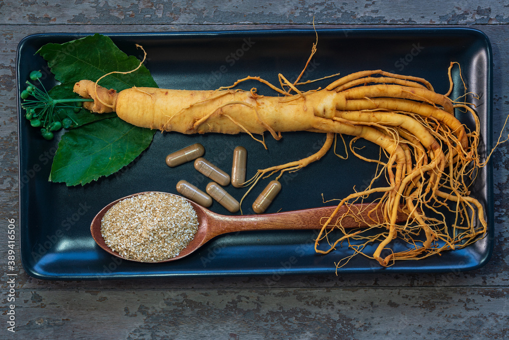 Wall mural Fresh ginseng root on black plate with powder for capsules medicine