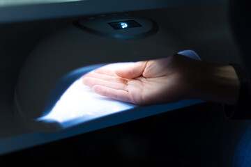 A woman at salon holding her hand under a uv led lamp .