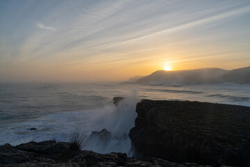 huge storm surge ocean waves crashing onto shore and cliffs at sunrise