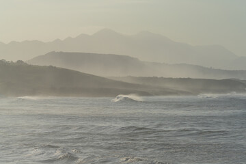 mountain landscape in silhouette with beach and waves breaking in the foreground