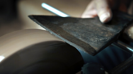 Asian man sharpening axe on a grinder