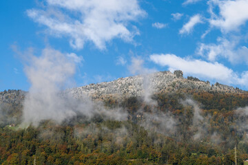 fall colors forest and mountain with snow at the top under a cloudy and misty sky