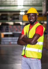 The engineer worker holds tablet crossed arm and standing in the automotive parts warehouse center. Man wears a safety helmet and vest. In background shelves with goods. Feeling smile and happy work.