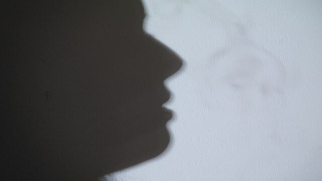 Woman smokes. 
Black shadow of Human on white wall.