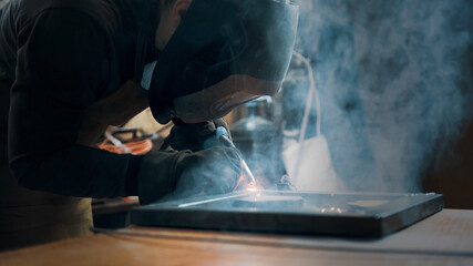 Worker wearing a mask and gloves soldering metal parts