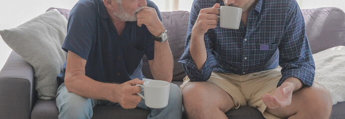Half portrait of two old father and son family relax talking and drinking coffees at sofa living...