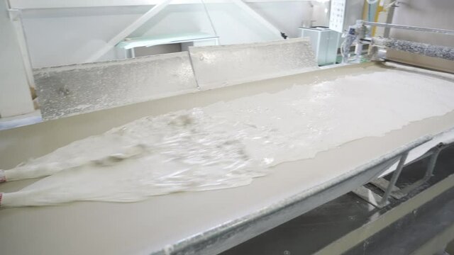 Feeding liquid gypsum to conveyor. Dissolved Gypsum flows on a machine or paper. Manufacturing plasterboard sheets or gypsum board by conveyor on factory. Production of building materials or drywall