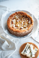 pie with dor blue cheese, pears and almond, whole round on a plate on a white table. Sugarless. Selective focus.