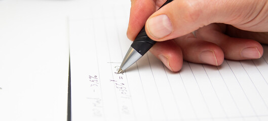 The student solves mathematical formulas. Man writes with a pen in a notebook.