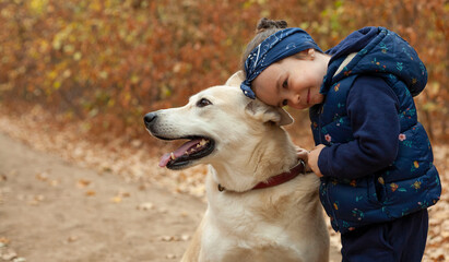 Little girl on a walk in the woods with a dog. The girl hugs the dog.