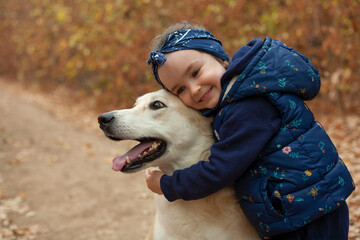 Little girl on a walk in the woods with a dog. The girl hugs the dog.