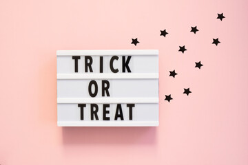Halloween flat lay of lightbox with Trick or treat text and decoration over pink background. Holiday greeting card, party flyer, invitation concept