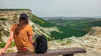 A girl tourist sits on a wooden bench on the top of the Crimean mountains, which offers a beautiful view. © Michael
