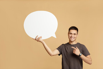 Smiling young guy with smart watch holds blank space for words in hand and points to abstract bubble