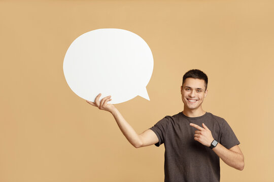 Smiling young guy with smart watch holds blank space for words in hand and points to abstract bubble