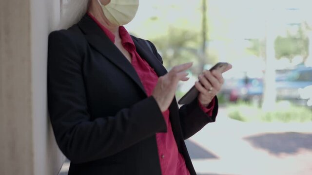 Scene moves up from a colorful plant to a woman wearing a mask due to COVID19 standing in an outdoor urban environment looking at her smartphone.