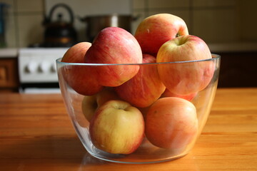 Apples in a glass bowl on a wooden table. Kitchen in the house.