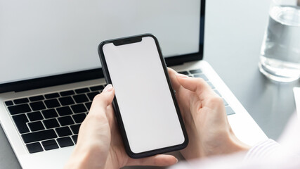 Close up young woman holding smartphone with big mock up white screen in hands, choosing mobile application, communicating in social network, web surfing useful information or playing online game.