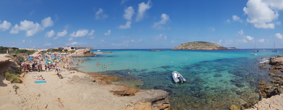 San Antonio, Ibiza - 07/14/2018: Panoramic view of Cala Comte beach in Spain during summer with a crispy clear turquoise sea water and people laying down on the sand beach