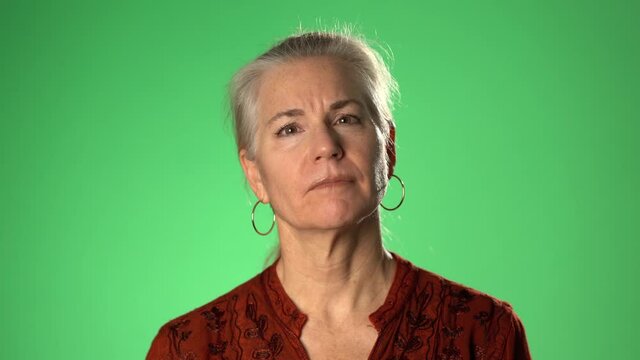 Smiling middle aged mature woman listening and looking at camera, lady making video blog or call at home, happy friendly senior vlogger sitting online, portrait. Isolated on green screen chroma key.