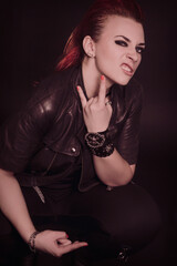 Portrait of a young punk woman with dark leather jacket isolated in studio on black background.
