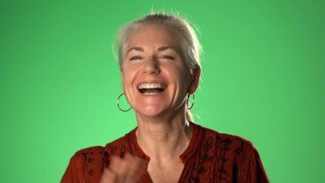 Smiling middle aged mature woman waving hand looking at camera, older lady video blog or call at home, happy friendly senior vlogger sitting on sofa, portrait. Isolated on green screen chroma key.