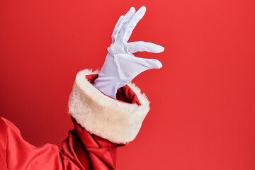 Hand of a man wearing santa claus costume and gloves over red background picking and taking...