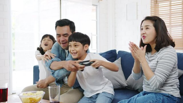Happy Asia family dad, mom and kids funny playing video game with technology console in living room at house. Self-isolation, stay at home, social distancing, quarantine for coronavirus prevention.