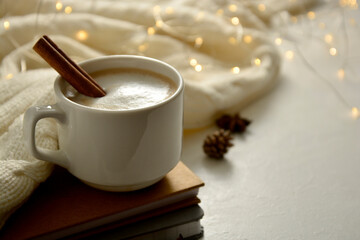 Obraz na płótnie Canvas Cup of coffee with cinnamon and foam, knitted scarf and bokeh lights. Winter abstract mockup. Copy space.