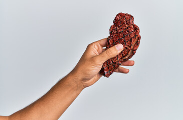 Hand of young hispanic man holding grilled beef over isolated white background.