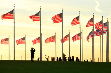 Silhouettes and U.S. national flags at Washington Monument grounds during sunset - Washington D.C....