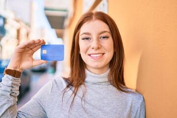 Young irish teenager girl smiling happy holding credit card at the city.